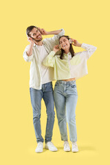 Happy young couple with headphones listening to music on yellow background