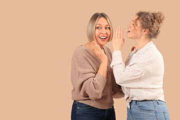 Beautiful shocked women in stylish jeans gossiping on beige background