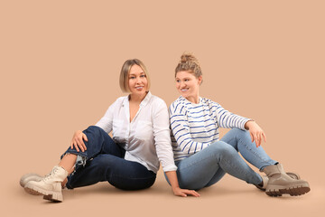 Beautiful happy women in stylish jeans sitting on beige background