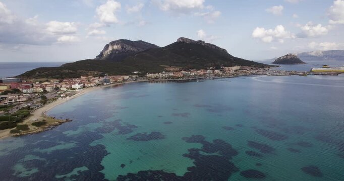 Coastal Town Of Golfo Aranci With Mountain Hikes In The Background In The Province of Sassari, Sardinia, Italy. Aerial Shot