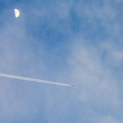 Plane flies pass over the moon on blue sky airplane trail