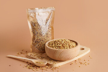 Bowl and pack with raw buckwheat grains on beige background