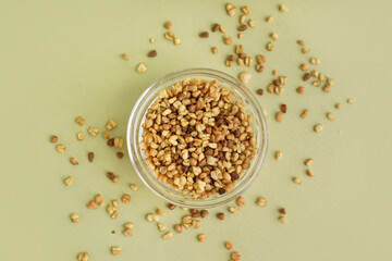 Glass with raw buckwheat grains on green background
