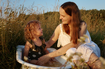 Little smiling adorable cheerful girl and her mother experiencing happiness while washing in...