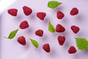 Raspberries and green leaves on pink background creating a vibrant contrast.