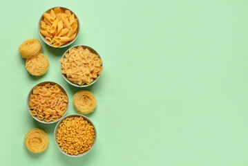 Bowls with different tasty uncooked pasta on green background