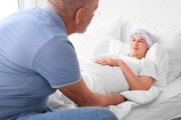 Mature woman after chemotherapy lying with her husband in bedroom