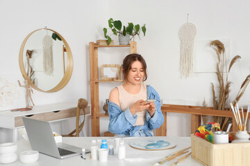Young woman taking picture of fluid art painting on table in workshop