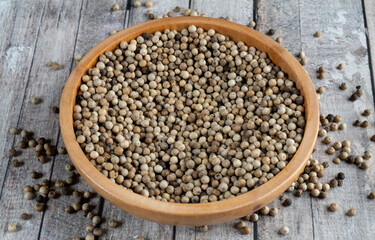 close shot of a wooden bowl of coriander seeds with scattered coriander seeds on table