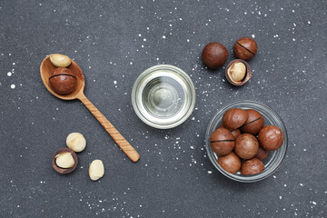 Bowls of oil with macadamia nuts and spoon on dark background