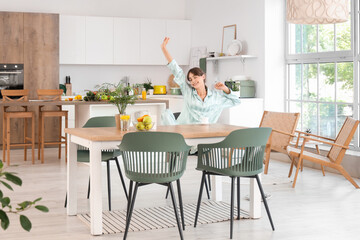 Sleepy young woman with cup of coffee sitting at table in dining room