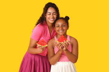 Beautiful young African-American woman and her cute daughter with pieces of fresh watermelon on yellow background