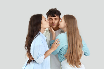 Young man with two women kissing on light background. Polyamory concept
