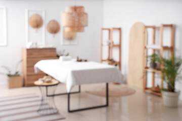 Blurred view of light spa salon with massage couch, fans and shelf units