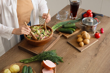 Young woman stirring okroshka at table in kitchen, closeup