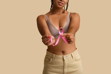 Young woman with pink ribbon on beige background, closeup. Breast cancer awareness concept