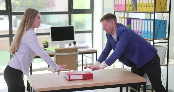 Man and woman push ring binder with report on table in office. Workers demonstrate unwillingness to perform work shifting responsibility