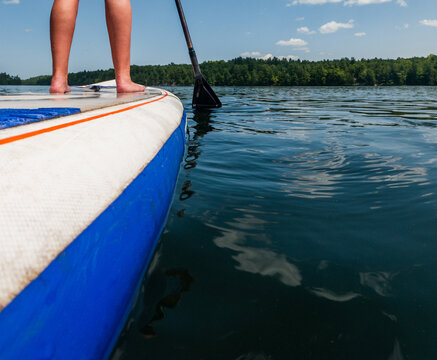 Legs of person standing on paddle board on a lake in summer.
