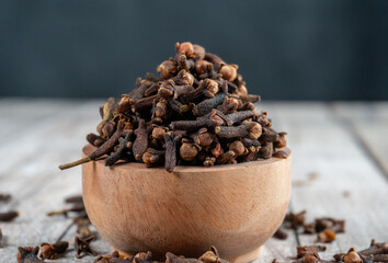 a wooden bowl filled dried cloves on wooden table with blurry background