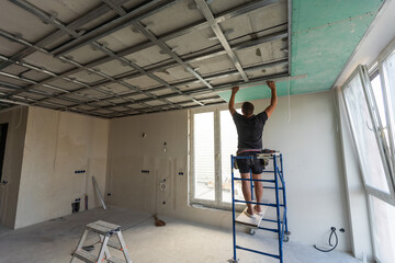 Workers fitting panel into frame of ceiling.