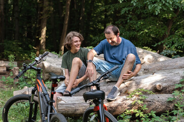 Fototapeta premium Father and his teenager son sitting in nature together with bicycles, talking and smiling