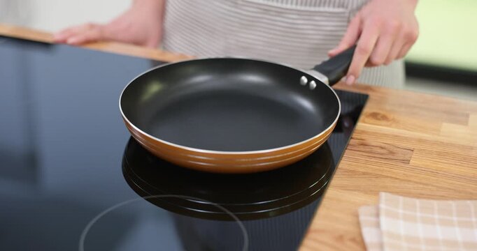 Young woman places frying pan on stove turning on at home. Housewife adjusts burner to heat up for meal preparation for family gathering