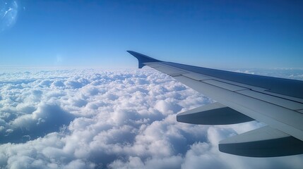 Obraz premium Expansive view of a clear blue sky with fluffy clouds from an airplane window, featuring a close-up of the wing for a travel-themed photo.
