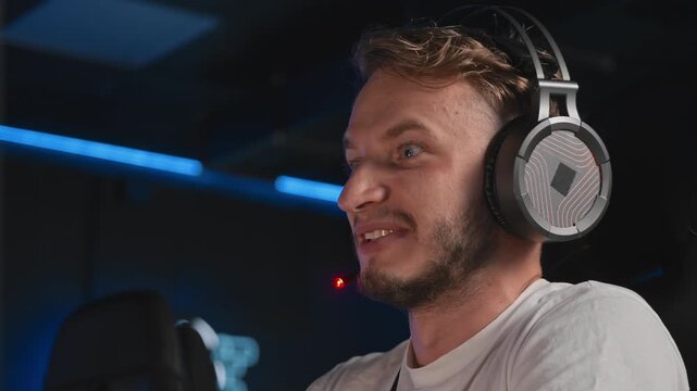 Happy smiling gamer emotionally plays tight game, facial expressions. Cyber player is playing shooter game on PC at cyber space cafe during cybersport tournament. Tactical shooter game, cybersport