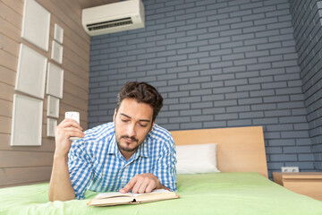 A man turns on the air conditioner on a hot summer day while reading a book, preparing for the new school year at university