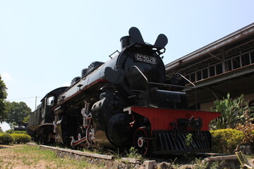 A vintage steam locomotive on display outdoors under the bright sun, showcasing historical rail transportation.