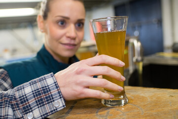 female quality control worker in brewery inspecting glass of ale