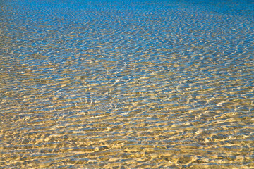 Crystal-clear sea water in a lagoon on tropical island Mauritius, Indian Ocean. Reflections of blue sky and refractions of bright sunlight on hallow sandy beach with perfect bathing conditions.