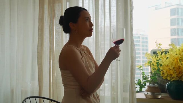 Beautiful woman holding glass, drinking and tasting red wine in winery while enjoying in front of the window