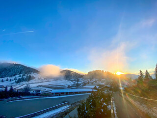 Winter Sunset Over Snow-Covered Hills in Transylvania. A stunning winter sunset over the snow-covered hills and old houses in Transylvania. The clear sky and setting sun illuminate the peaceful.