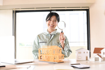 住宅模型の前で虫眼鏡を持つ作業服姿の女性