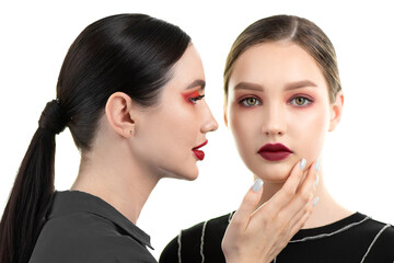 Two young beautiful women with bright red makeup are posing together. Models with perfect skin and artistic make-up, red lips and red eye makeup. Beautiful female portrait.