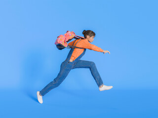 Girl Leaping with Backpack on Isolated Blue Background