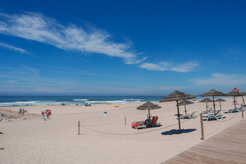 A tranquil beach in Portugal featuring a sandy shore, clear blue sky, and a wooden boardwalk....