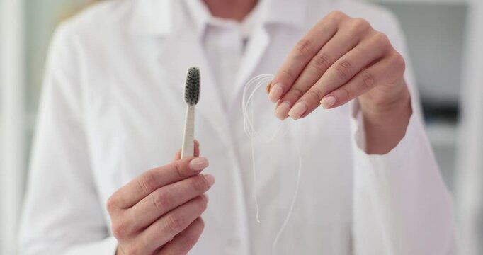 Female dentist presents toothbrush and floss to patient. Female doctor demonstrates essential tools for daily oral hygiene during consultation
