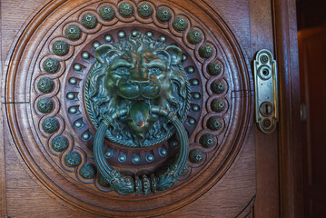 A detailed bronze or brass lion's head door knocker with ornate carvings on a wooden door in Sintra, Portugal, showcasing historical architectural craftsmanship.
