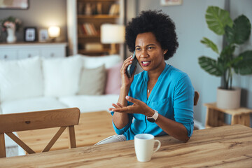 Portrait of mid adult woman sitting on the chair in the living room and talking on the phone. African American woman making a phone call.