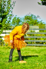 Young Girl in Yellow Puffer Jacket Raising Pumpkin in Lush Garden During Autumn