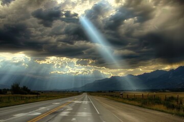Sunbeam breaking through stormy clouds over an empty highway with mountains in the distance.