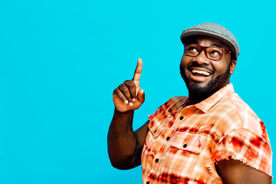 Portrait of a happy man in orange shirt smiling and pointing up, with blue copy space around him