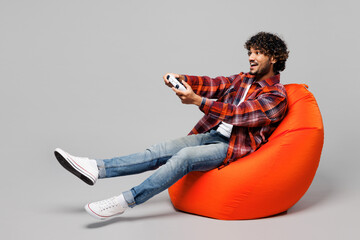 Full body young happy Indian man he wears red shirt casual clothes sit in bag chair hold in hand...