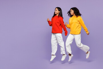 Obraz premium Full body side view two young happy little kid teen girls women they wear red yellow hoodie casual clothes jump high run fast look aside isolated on plain pastel purple background. Lifestyle concept.