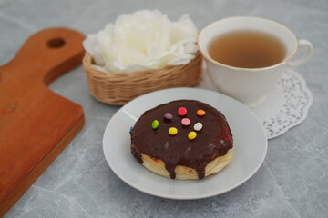 Donut with chocolate glaze and cup of tea on the table