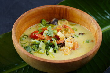 Tom Yam kung Spicy Thai soup with shrimp, seafood,tomatoes, mushrooms, lemongrass, coconut milk, ginger and chili pepper in bowl . Traditional Thai food