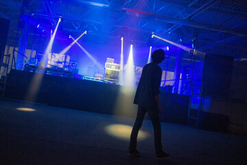 A DJ performs on a stage bathed in blue light, surrounded by music equipment and illuminated by multiple spotlights. The atmosphere is electric and energetic the essence of a live performance.