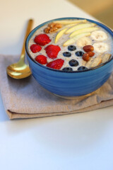 Bowl filled with healthy smoothie, fruit pieces and nuts on the table. Selective focus.